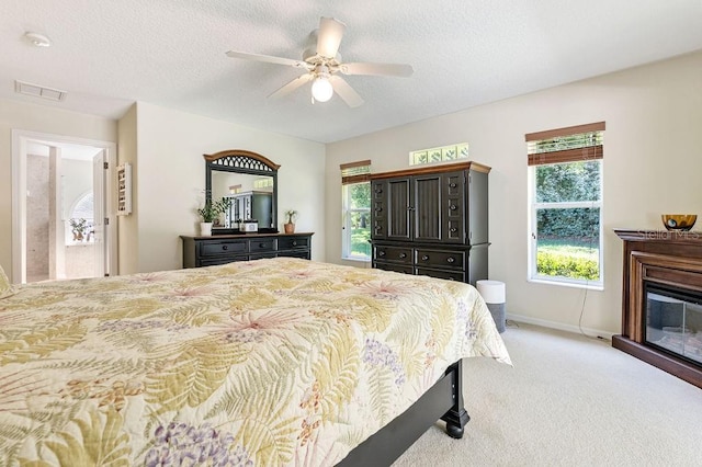 bedroom featuring visible vents, baseboards, a glass covered fireplace, light colored carpet, and ceiling fan