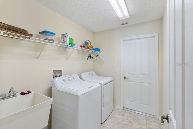 clothes washing area featuring a sink, a textured ceiling, light tile patterned flooring, washing machine and dryer, and laundry area