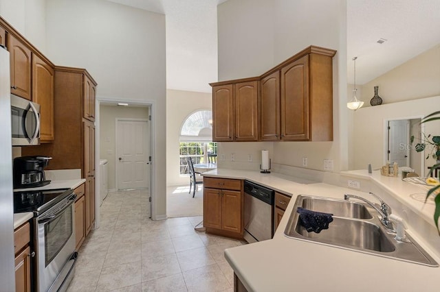 kitchen with stainless steel appliances, light countertops, a sink, decorative light fixtures, and high vaulted ceiling