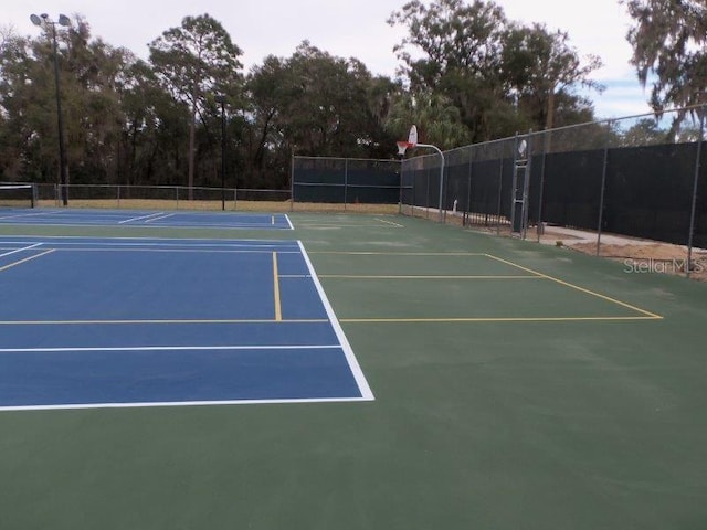 view of tennis court featuring community basketball court and fence