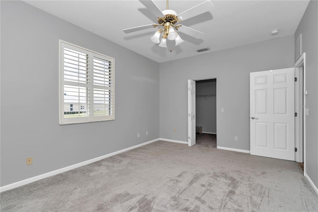 unfurnished bedroom with visible vents, baseboards, a ceiling fan, a walk in closet, and carpet flooring