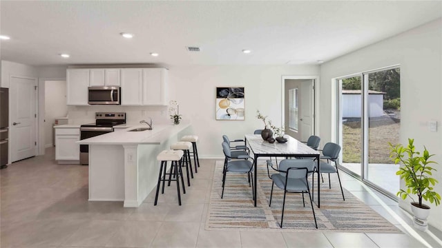 kitchen with appliances with stainless steel finishes, light countertops, a kitchen breakfast bar, white cabinetry, and visible vents