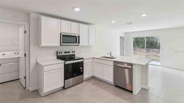 kitchen featuring a peninsula, washer / clothes dryer, light countertops, a sink, and appliances with stainless steel finishes