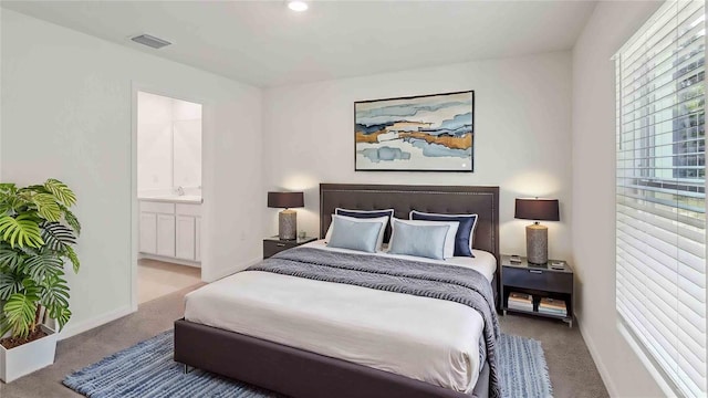 carpeted bedroom with a sink, visible vents, multiple windows, and ensuite bathroom