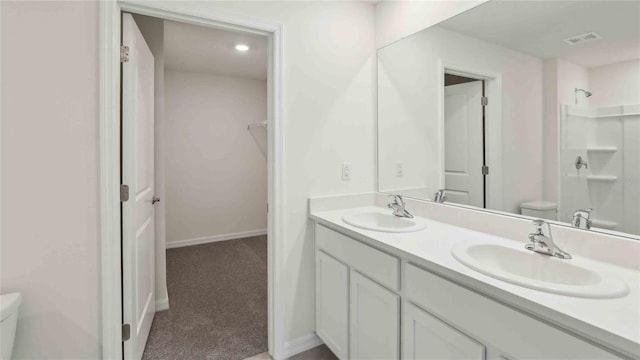 bathroom featuring double vanity, a sink, walk in shower, and toilet