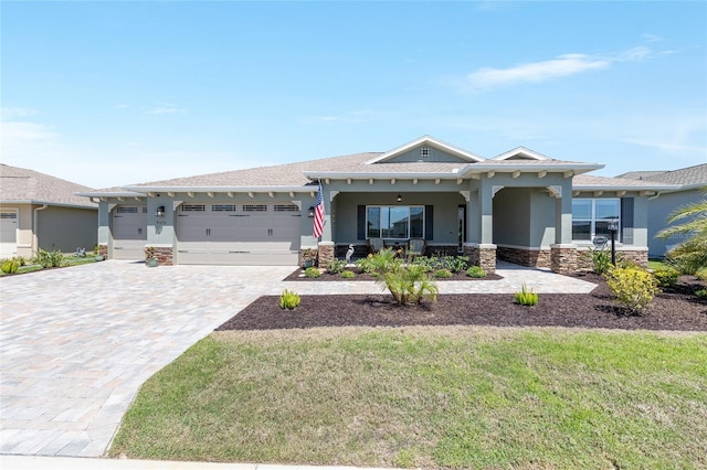 view of front facade with an attached garage, stone siding, covered porch, stucco siding, and decorative driveway
