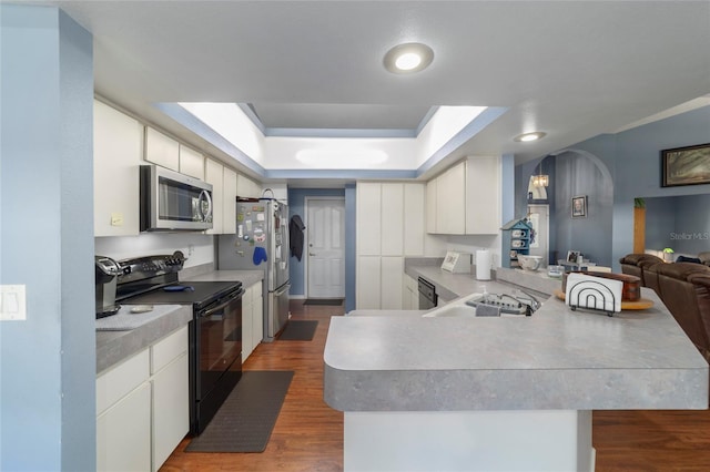 kitchen with a tray ceiling, arched walkways, a peninsula, dark wood-style flooring, and stainless steel appliances