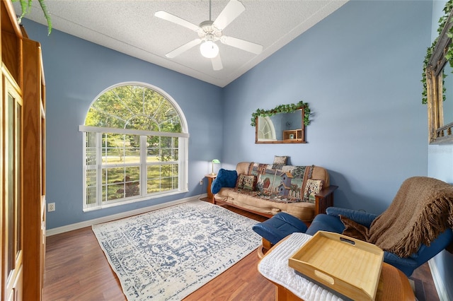 living room with baseboards, ceiling fan, a textured ceiling, wood finished floors, and lofted ceiling