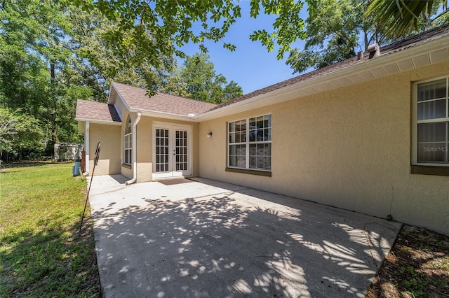 back of property with a patio, roof with shingles, stucco siding, french doors, and a lawn