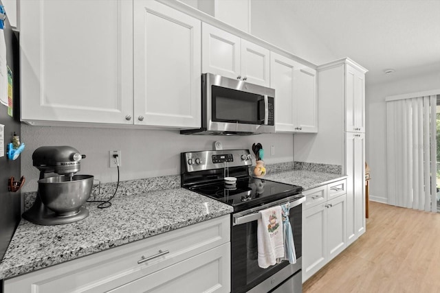 kitchen with light stone countertops, light wood-style flooring, white cabinetry, and appliances with stainless steel finishes