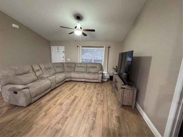 living area with light wood finished floors, a ceiling fan, baseboards, and a textured ceiling