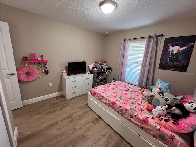 bedroom featuring light wood-style flooring, a textured ceiling, and baseboards