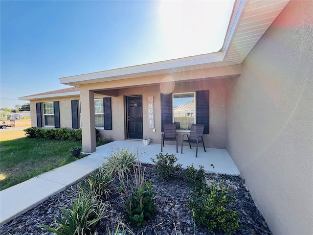 view of exterior entry with a porch, a yard, and stucco siding