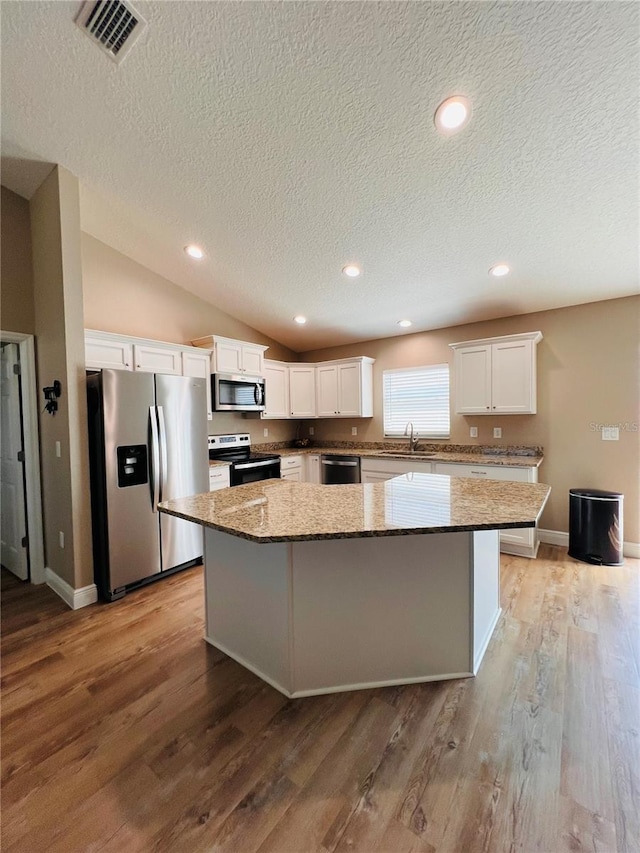 kitchen featuring stainless steel appliances, a center island, a sink, a textured ceiling, and visible vents
