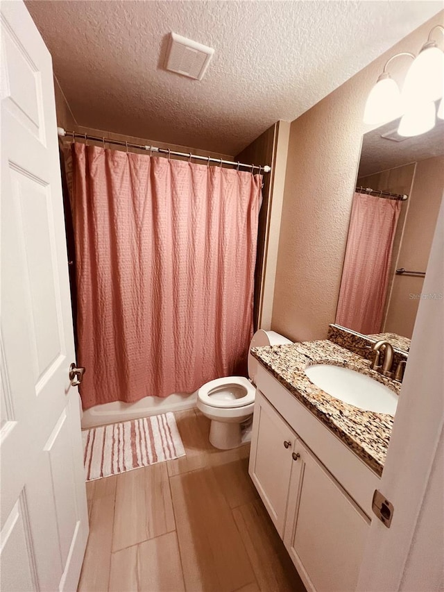 bathroom with a textured wall, visible vents, toilet, vanity, and a textured ceiling
