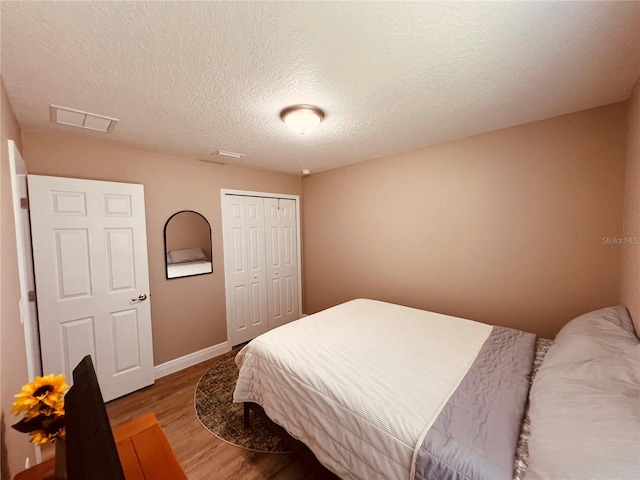 bedroom with light wood-style flooring, a textured ceiling, baseboards, visible vents, and a closet