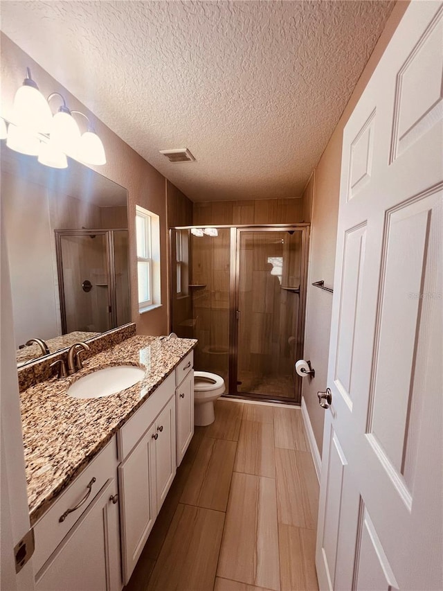 full bathroom featuring a textured ceiling, toilet, visible vents, a shower stall, and vanity