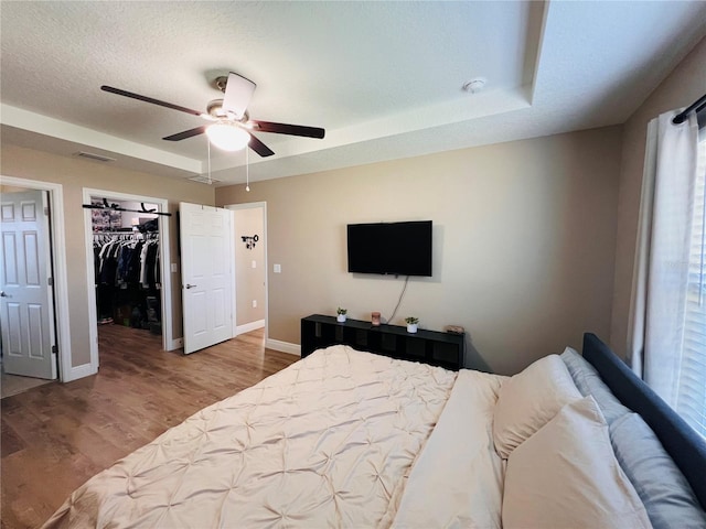 bedroom with wood finished floors, visible vents, a ceiling fan, a walk in closet, and baseboards
