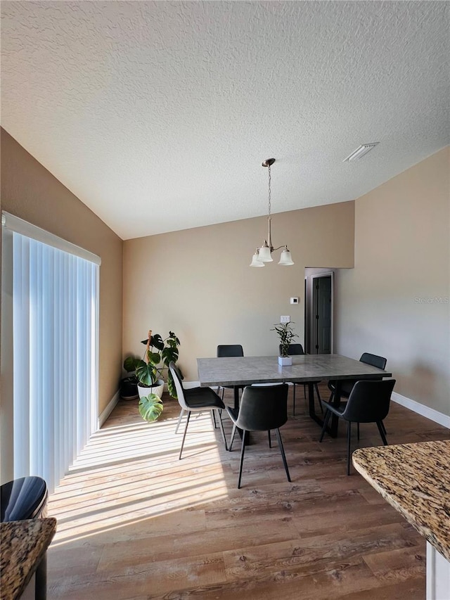 dining area featuring lofted ceiling, wood finished floors, a textured ceiling, and visible vents