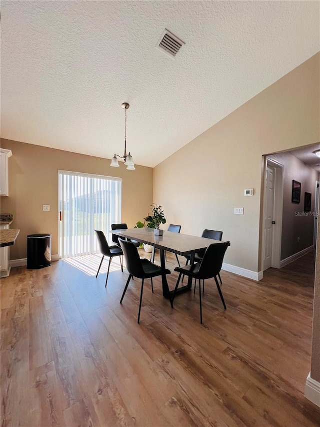 dining space featuring an inviting chandelier, light wood finished floors, a textured ceiling, and visible vents