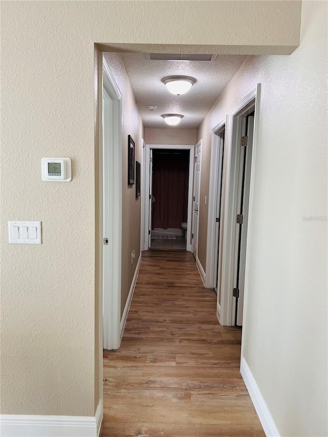 hall featuring light wood-style flooring, a textured ceiling, and baseboards