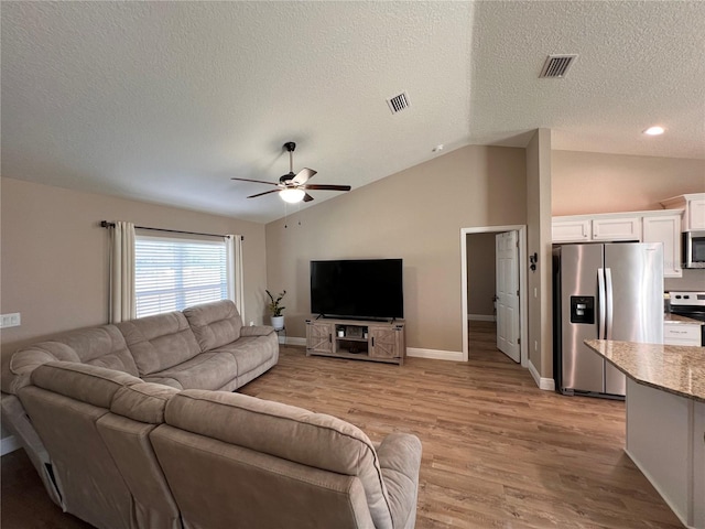 living area with vaulted ceiling, a ceiling fan, a textured ceiling, light wood finished floors, and visible vents