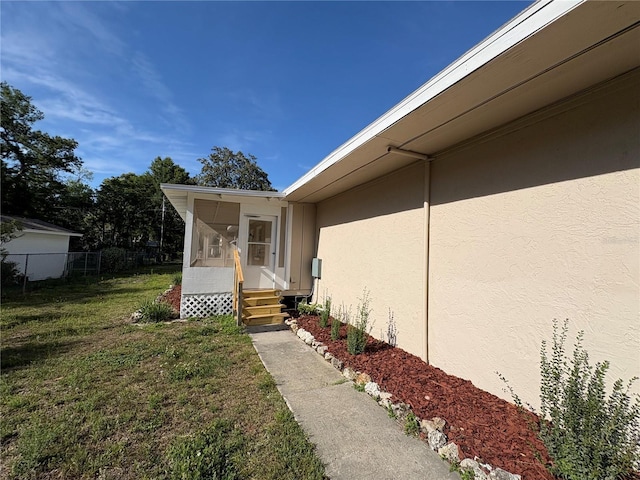entrance to property featuring a yard, fence, and stucco siding