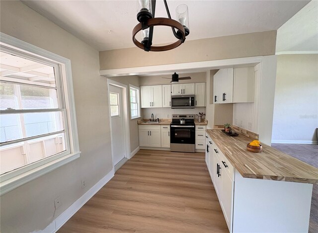 kitchen with baseboards, white cabinetry, butcher block counters, light wood-style floors, and appliances with stainless steel finishes