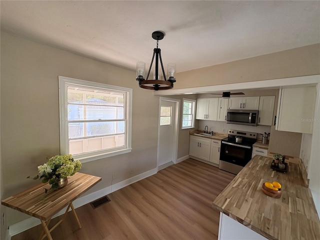 kitchen with light wood-style floors, butcher block counters, a chandelier, a sink, and stainless steel appliances