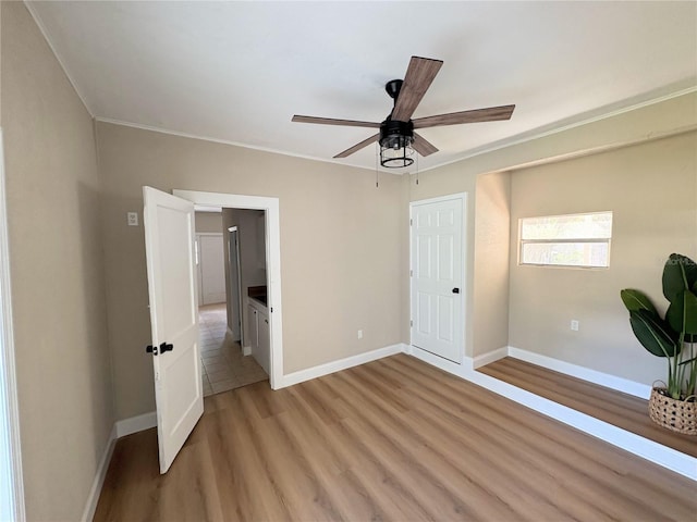 unfurnished bedroom with crown molding, baseboards, light wood finished floors, and a ceiling fan
