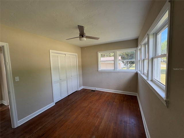unfurnished bedroom featuring dark wood-type flooring, a closet, baseboards, and ceiling fan