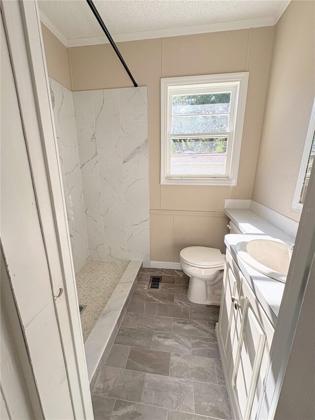 bathroom featuring a textured ceiling, tiled shower, vanity, visible vents, and toilet
