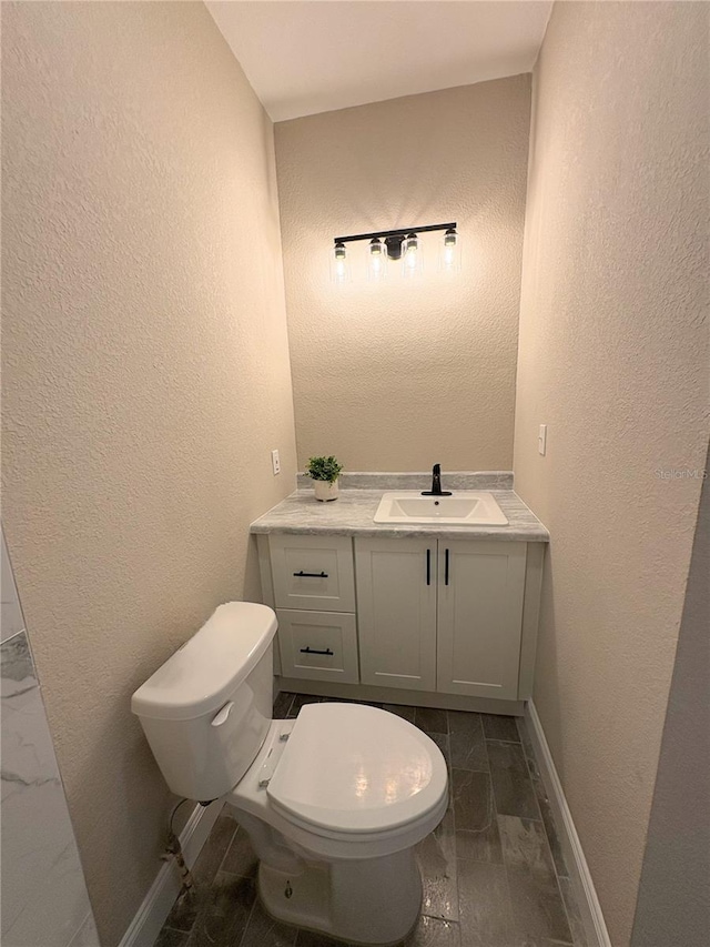 bathroom featuring vanity, baseboards, a textured wall, toilet, and marble finish floor