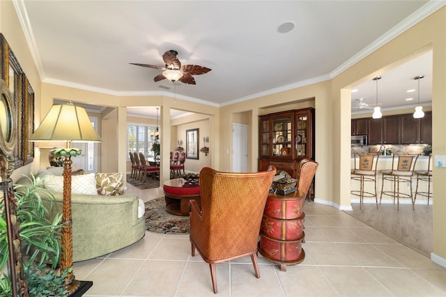 living area with ornamental molding, baseboards, ceiling fan, and light tile patterned floors