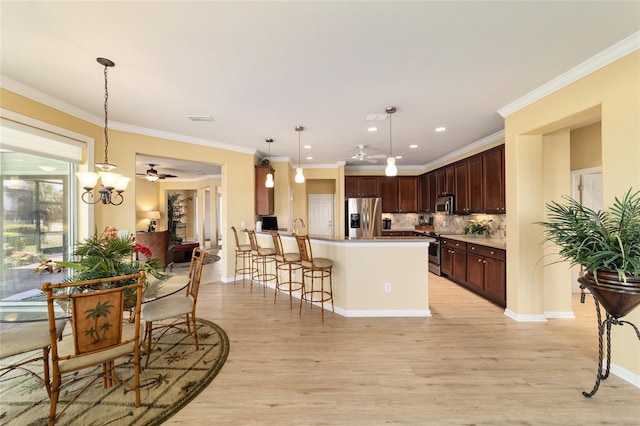 kitchen featuring light wood-type flooring, a peninsula, a kitchen bar, appliances with stainless steel finishes, and ceiling fan with notable chandelier