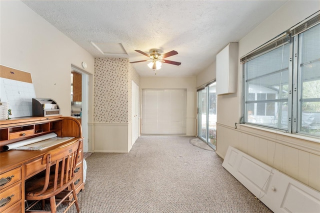 interior space with wainscoting, light carpet, a ceiling fan, and a textured ceiling