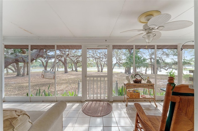 sunroom / solarium with tile patterned floors, a ceiling fan, a water view, and a healthy amount of sunlight
