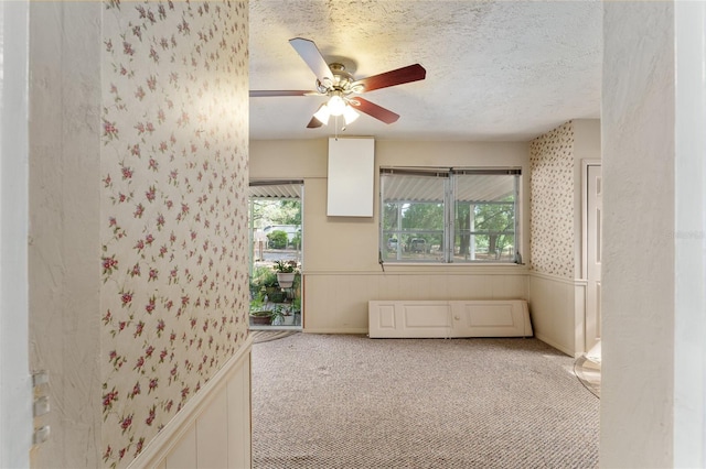 spare room featuring wallpapered walls, carpet, a wainscoted wall, a ceiling fan, and a textured ceiling