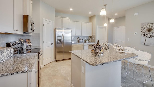 kitchen featuring an island with sink, a kitchen breakfast bar, white cabinetry, light stone counters, and stainless steel appliances