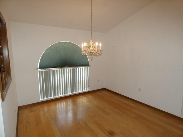 unfurnished room with a notable chandelier, baseboards, and wood finished floors