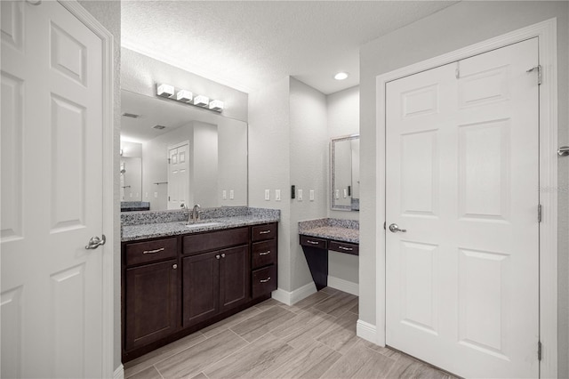 full bath with baseboards, vanity, a textured ceiling, and recessed lighting