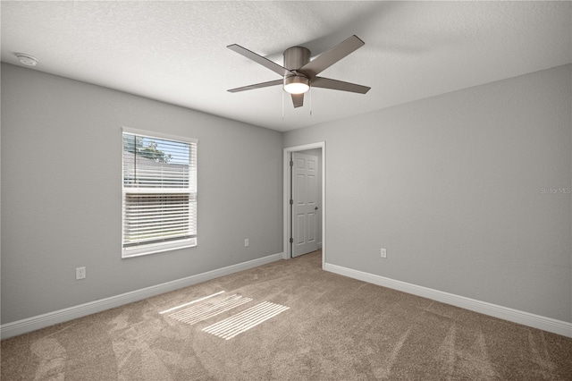 spare room featuring a textured ceiling, a ceiling fan, baseboards, and light carpet