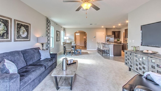 living room featuring baseboards, recessed lighting, a ceiling fan, arched walkways, and light colored carpet