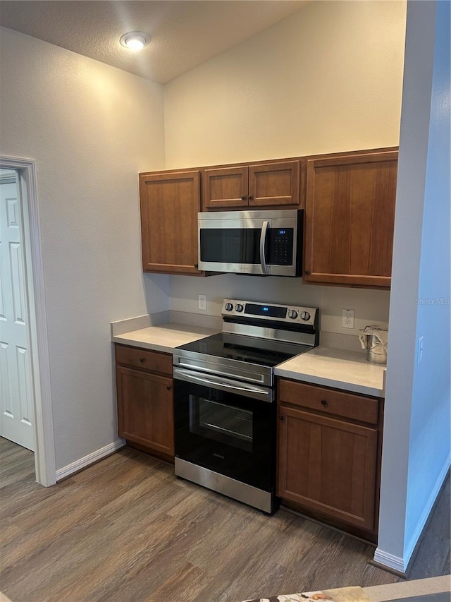 kitchen featuring baseboards, wood finished floors, stainless steel appliances, and light countertops
