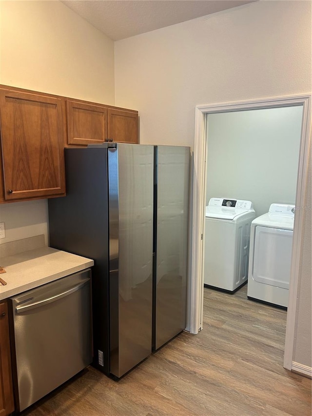 kitchen with brown cabinets, light wood-style floors, stainless steel appliances, light countertops, and washing machine and dryer