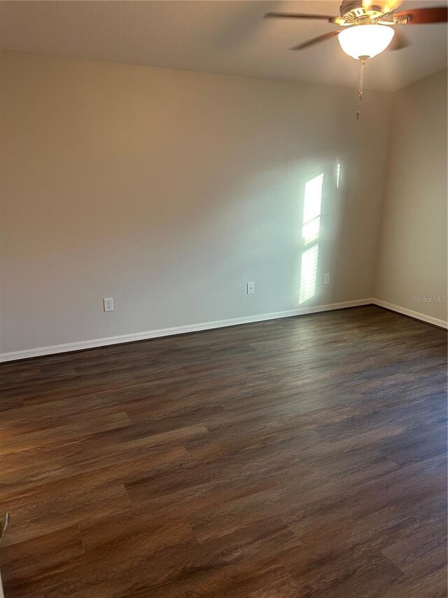 unfurnished room featuring baseboards, a ceiling fan, and dark wood-type flooring