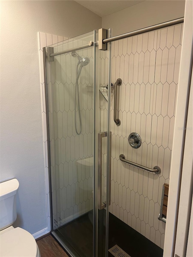 bathroom featuring baseboards, wood finished floors, a shower stall, and toilet