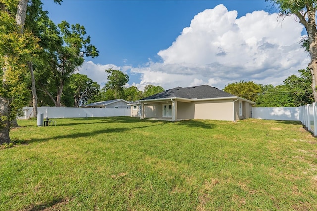 rear view of house with a lawn, stucco siding, and a fenced backyard