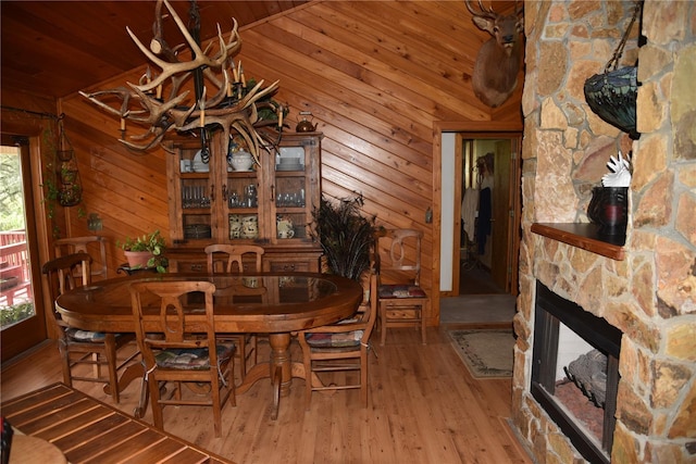 dining area featuring a stone fireplace, wooden ceiling, wood walls, and wood finished floors