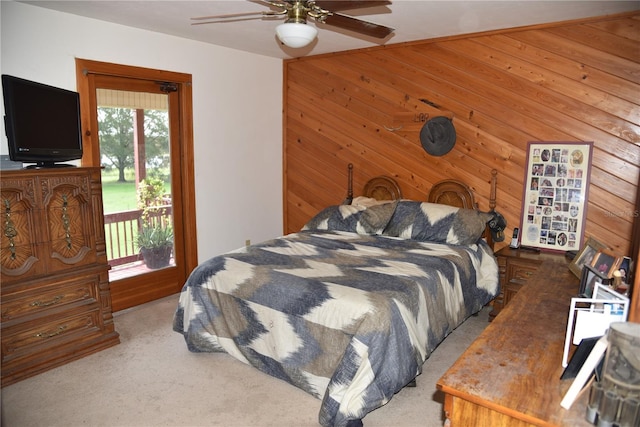 carpeted bedroom with wooden walls, access to exterior, and a ceiling fan